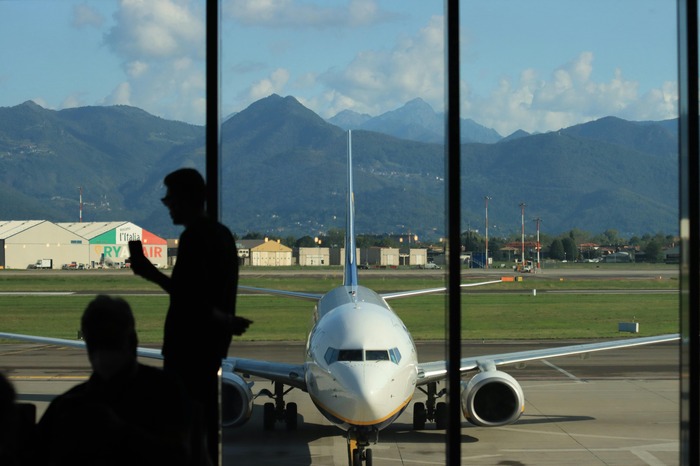 Kroz prozor čekaonici vidi se avion parkiran na pisti sa zelenim brdima u pozadini