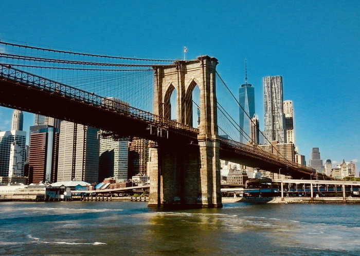 Pogled na Brooklyn Brige sa strane Brooklyn-a, u pozadini Manhattan i plavo nebo.