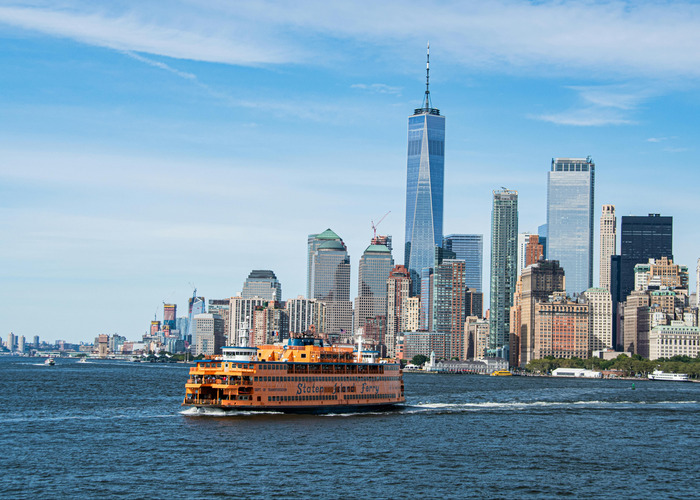 Žuti Staten Island trajekt koji plovi prema Manhattanu u pozadini.