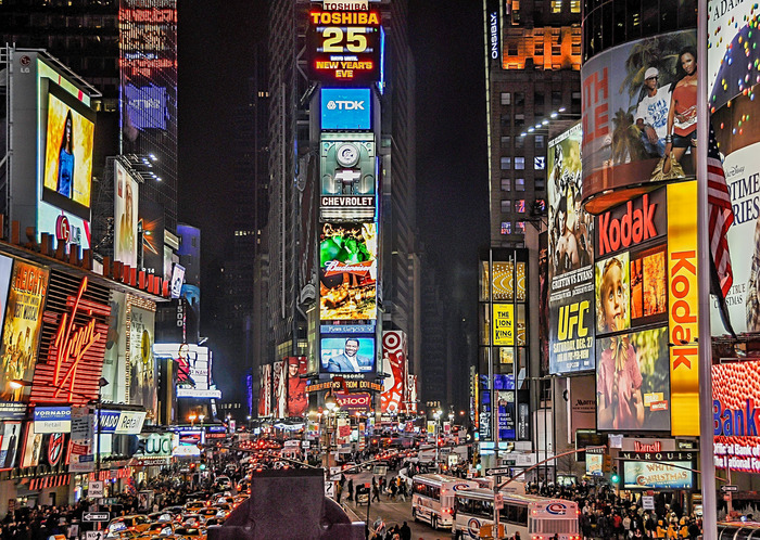 Times Square u noći, reklame obasjavaju trg koji je pun auta i ljudi.