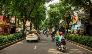 Što raditi u Ho Chi Minhu? Ulica u Ho Chi Minhu sa skuterima u autima. Zeleno drveće uz cestu.