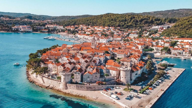Stari grad Korčula iz zraka, narančasti krovovi i plavo more.