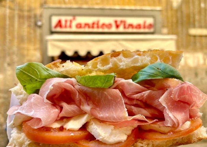 Sendvič s pršutom u prvom planu, u pozadini natpis All'Antico Vinaio