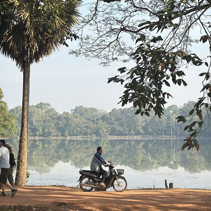 A man on a bike in Angkor Wat, passing by a lake.