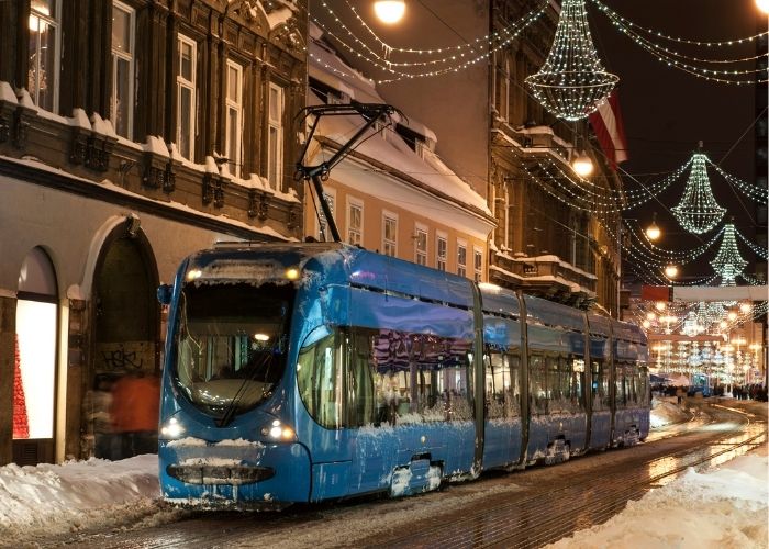 Blue tram on Zagreb Christmas Market, snow around the street.