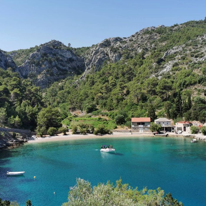 Šljunčana plaža, borovi, kuće i plavo more