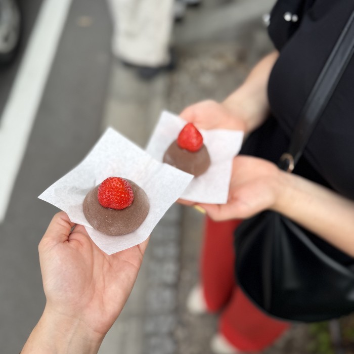 Dvije ženske ruke drže čokoladni mochi s jagodom u ruci