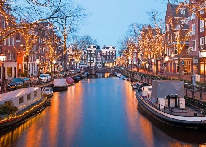 Osvijetljene kuće i brodice uz amsterdamski kanal u sumrak.