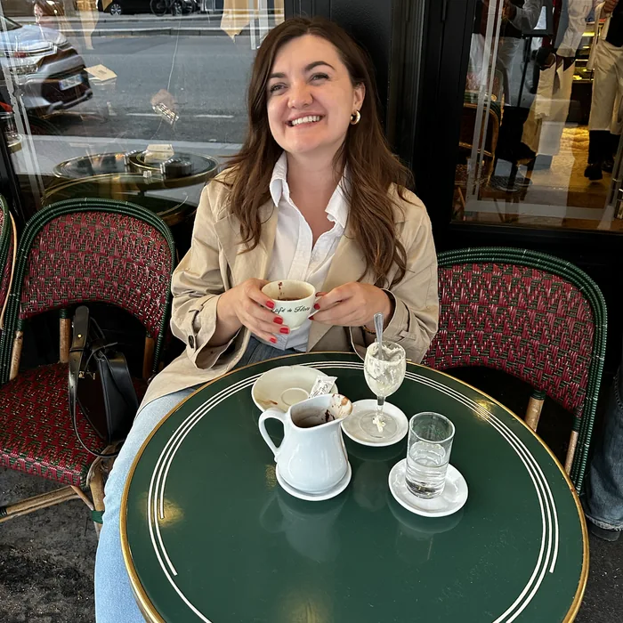 Ana sjedi na terasi Café de Florea i drži šalicu tople čokolade