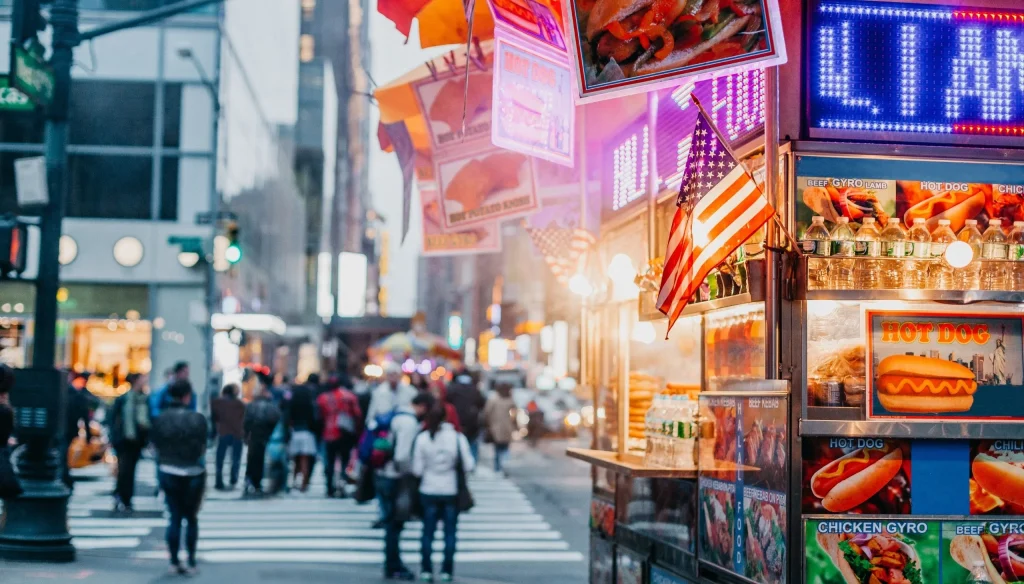Ulični štand s hot dogovima i američkom zastavom na prometnoj ulici u New Yorku.