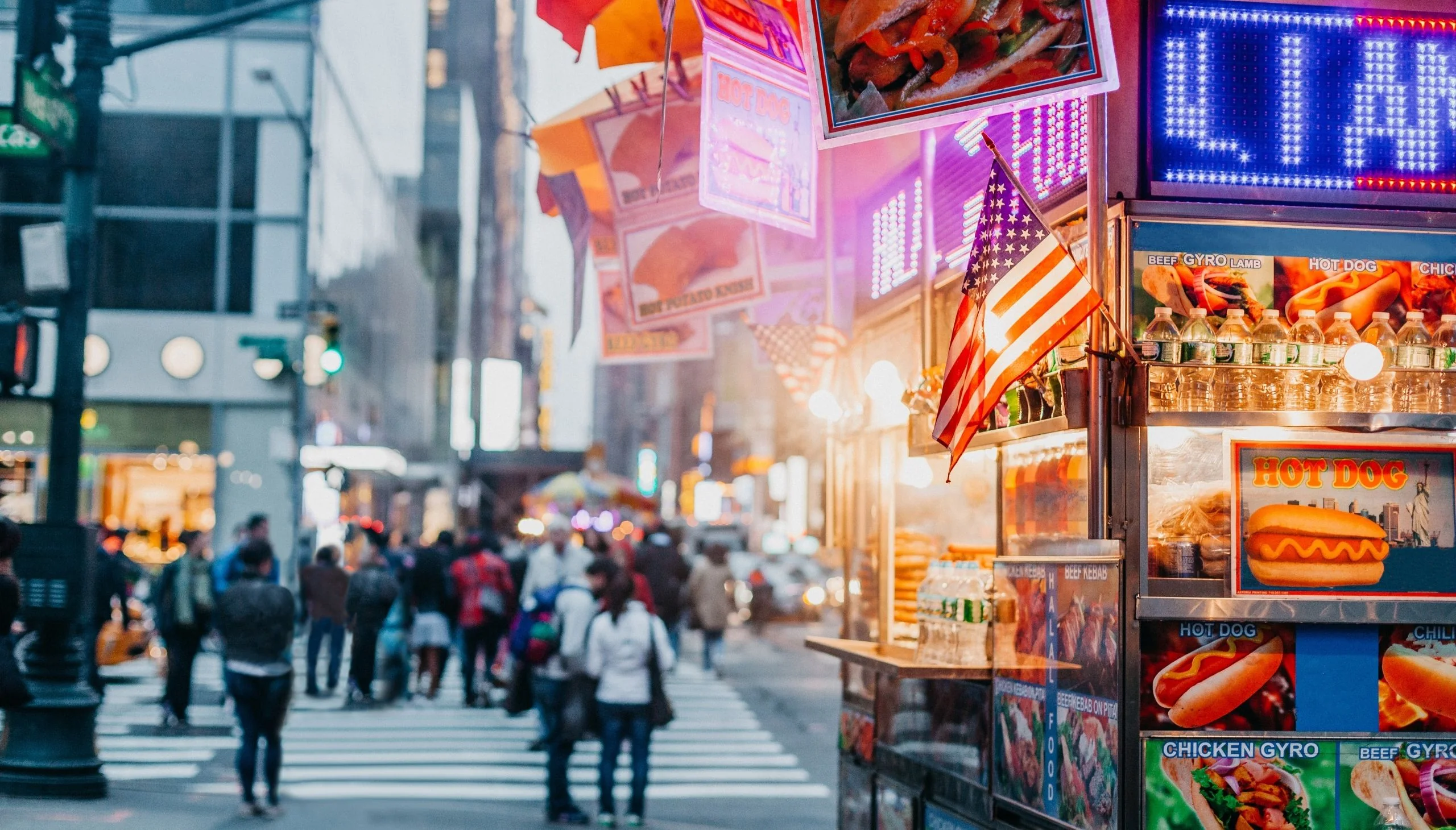 Ulični štand s hot dogovima i američkom zastavom na prometnoj ulici u New Yorku.